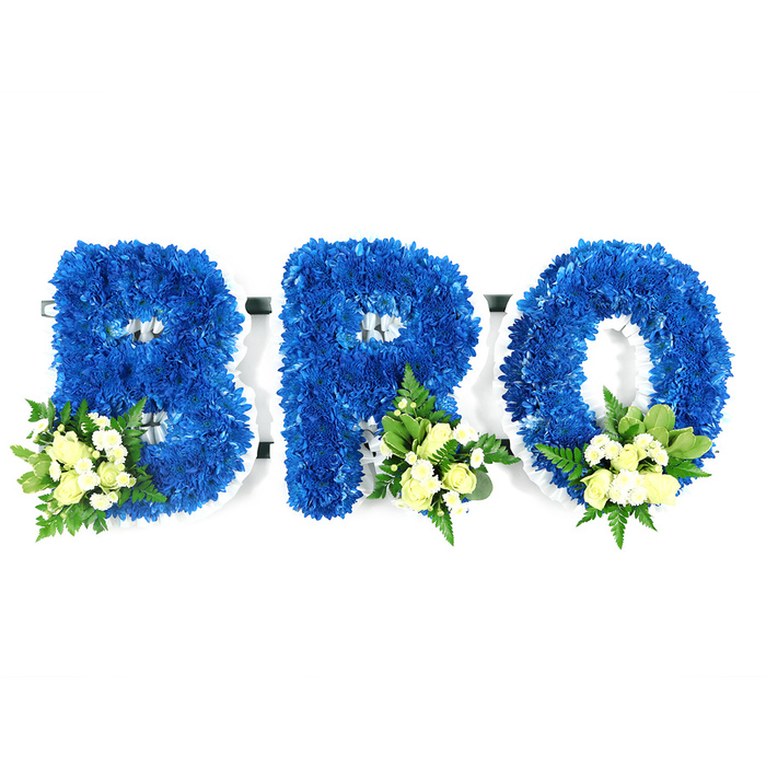 A carefully composed studio image presents three standalone letters-B, R and O-each crafted from a dense carpet of radiant royal blue chrysanthemums. Shot at eye level on a pristine white background, the letters appear sculptural and tactile, their rounded forms defined by tightly clustered petals that create a lush, almost velvety surface. Soft accent clusters sit at the lower sections of each letter: cream or pale yellow spray roses in mixed bloom stages, intermingled with small white filler flowers such as tiny mums or baby's breath, and framed by rich green foliage ranging from broad glossy leaves to delicate, fern-like sprigs. The white foam base or thin frame peeks through at the inner edges and negative spaces, speaking to the careful construction and support beneath the floral mass. The saturated blue tone carries connotations of calm, fidelity and remembrance, while the ivory accents lend a gentle purity and warmth-together they form a visual language of solace and respect. The arrangement's subtle scent blends rose sweetness with the fresh green note of foliage, and the soft studio lighting highlights both depth and detail. Intended as a personalised funeral tribute, this BRO composition is suited to memorial services, church viewings, or graveside placements. For relatives and friends in Stanmore, its dignified presence would be fitting for delivery to local chapels, community funeral directors near Stanmore Tube, or family homes along Stanmore High Street and the surrounding streets, offering a composed and heartfelt expression of sympathy.
