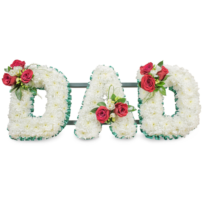 A deeply respectful, custom-made sympathy tribute spells the word DAD in three large block letters, each entirely cloaked in hundreds of small white chrysanthemum blooms that form a uniform, pillow-soft surface. The crispness of the white is set against a vivid emerald-green pleated ribbon that traces the perimeter of every letter, lending formal definition and a classic silhouette under soft studio lighting. Artfully placed floral clusters punctuate each letter: the left D is graced on its upper curve by several fully opened deep red roses paired with delicate white freesia and rich green foliage; the central A carries a similar arrangement positioned near its lower left stem, with an elegant loop of bright green bear grass providing a contemporary lift; the right D mirrors the first, completing a balanced, symmetrical composition. Slim, dark-green support bars run behind the letters, faintly visible and ensuring the display's cohesion without intruding on the flowers' quiet dignity. The white chrysanthemums suggest devoted remembrance while the red roses convey deep affection - together forming a language of honour suited to a father's memorial. As a local design from Flowers Stanmore, this piece is conceived with neighbourhood sensibilities in mind - appropriate for a service near Bentley Priory or a family farewell at the local crematorium - and reflects a skilled hand that arranges for both visual impact and tactile softness. It reads as both personal and ceremonial, an eloquent floral expression of loss, respect and lasting love.