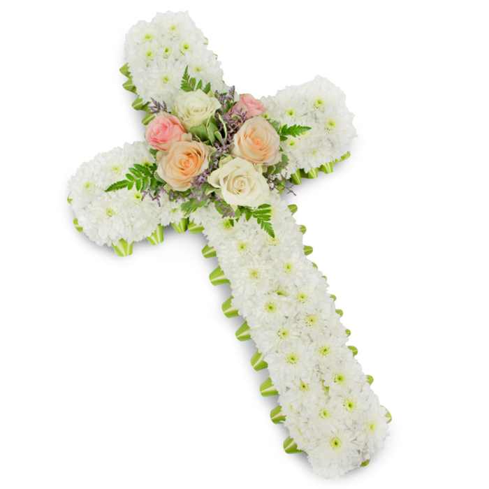 A stately floral cross, intended as a sympathy tribute, dominates the frame against a completely white background that emphasises its shape and detail. The cross is formed in the traditional Christian style, its vertical and horizontal arms proportioned with care, then entirely cloaked in crisp white chrysanthemums. The flowers appear to be small, button-shaped blooms, placed so close together that they create a uniform, velvety texture from top to base. This unbroken expanse of white suggests innocence, grace, and a peaceful, prayerful silence. Just visible along the edges is a trim of lime green ribbon, meticulously wrapped to follow every contour. Its fresh, bright tone outlines the silhouette, adding clarity and a contemporary lift to the design, while still allowing the white flowers to remain the focus. At the intersection of the beams, a cluster of roses serves as a gentle focal point. Fully open blooms in shades of soft blush pink, delicate peach, and creamy white nestle together, their petals layered like fine silk. They are framed by light, feathery fronds of fern and speckled with small hints of lavender-tinted filler flowers, which lend dimension and a touch of cool colour to the centre. The lighting is even and soft, revealing every curve and texture without distraction. This floral cross would feel perfectly suited to a Stanmore funeral or memorial service, perhaps placed near the front of a chapel or beside a photograph of the departed, offering a graceful symbol of faith, remembrance, and the enduring warmth of family ties.