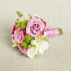 A compact, elegant bouquet lies horizontally on a softly textured, light beige fabric that looks like fine linen spread across a reception table. The arrangement is carefully composed, as if ready to be lifted for a Stanmore ceremony just off Church Road, its colours and textures balanced with a florist's practiced eye. Three open pink roses form the focal point, their blooms generous and velvety. Each rose shows a gentle gradient, transitioning from a pale, blush centre to petals edged with a richer, almost magenta-pink tone, giving the impression of softly brushed watercolour. Between and around these roses, bright lime green button chrysanthemums tuck in like rounded cushions, their tiny, densely packed petals creating a crisp, textured contrast that livens up the design. Delicate white and cream blooms, likely lisianthus or freesia, weave through the bouquet, their light, ruffled petals softening the overall shape and lending a sense of airy movement. Here and there, you can see petite star-shaped white flowers with warm yellow hearts, echoing the look of waxflower and adding subtle, intricate detail. On the right, the neatly gathered stems are bound into a short handle wrapped in smooth, fuchsia pink satin ribbon, gleaming softly as it catches the light. Over this, a slender strand of white faux pearls is wrapped in a gentle diagonal pattern, making the handle look like a piece of jewellery crafted to match the flowers. The neutral background, with its visible weave, serves as a calm stage that lets the pinks, greens, and creams stand out clearly. The overall feeling is one of refined romance and quiet joy, ideal for a bridesmaid, a civil ceremony bouquet at Stanmore's local venues, or an intimate engagement celebration at home.