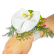 A delicate white Phalaenopsis corsage rests on a fair-skinned wrist against a clean, bright white background, every detail arranged with quiet care. The orchid dominates the composition: broad, smooth petals of pristine white unfold like satin, while the central labellum offers a small, sunlit blush of yellow with a deeper golden-orange throat that draws the eye. Beneath the bloom, feathery asparagus fern sprays fan out in fresh, bright green, their fine, lace-like texture softening the silhouette and lending a natural, floating quality to the piece. To the upper right of the orchid a clustered vein of Hypericum berries provides an autumnal counterpoint - glossy beads that graduate from pale green through warm rose into a rich cranberry red, suggesting ripeness and movement. A touch of ruffled lime-green accent foliage tucks in near the berries, adding a crisp, modern highlight. The corsage is secured on the wrist by a multi-strand bracelet of small, luminous white pearls; their cool, satiny surface contrasts with the orchid's velvety petals and sits comfortably against the skin. In gentle daylight the composition reads as timeless and romantic - soft to touch, subtly scented, and exquisitely balanced between formal elegance and organic charm. As a florist working in Stanmore near Stanmore Broadway and Canons Park, I would recommend this piece for weddings, prom, or any occasion where a single, sophisticated floral statement is desired. The pristine backdrop and careful styling let the colours and textures sing, while the overall mood remains one of quiet celebration and thoughtful craftsmanship.