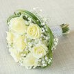 Presented on a warm, light beige fabric that softens the scene, this elegant hand-tied bouquet places seven substantial cream roses at its heart, each blossom at a slightly different point in its opening so the arrangement feels natural and alive. Nestled between and above the roses are clusters of delicate white gypsophila, their tiny buds forming a cloud-like veil that cushions the larger blooms and adds a whisper-light texture. Arcs of deep green bear grass have been ribboned through the design, looping with graceful confidence to frame each rose and introduce a contemporary, botanical energy that suggests a spring meadow. The bound stems create a neat, secure handle wrapped in silvery satin; neat rows of tiny pearls embellish the ribbon, offering a soft, opulent note without overpowering the bouquet's understated tones. The photograph is lit with even, diffuse light that brings out the creamy warmth of the petals and the fresh sheen of the foliage, while the neutral linen backdrop ensures the composition reads pure and refined. Close your eyes and you might detect the roses' faint, sweet perfume balanced by the cool, green scent of cut grass-an aroma that pairs beautifully with a morning ceremony in the Stanmore Hill area or an intimate registry room on Stanmore Broadway. This bouquet was composed with an eye for timeless bridal style, merging traditional romance with a hint of modern texture, suitable for weddings, anniversaries, or a composed sympathy tribute delivered across the local community.