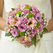 In this image, an exquisite hand-tied bouquet evokes the quiet elegance of a Stanmore wedding, poised between tradition and modern style. The heart of the arrangement is formed by lilac and dusky mauve roses, their petals densely layered into perfect spirals that invite the fingertips, each bloom a soft whirl of colour from silvery lavender at the edges to a richer mauve at the centre. Nestled among them are fine sprays of gypsophila, or baby's breath, their delicate white blossoms clustering in airy tufts that lend the bouquet a weightless, almost floating quality. Scattered thoughtfully throughout, bright green button chrysanthemums provide a vivid contrast; their compact, rounded shapes and lively chartreuse tones bring a playful spark, as fresh and energising as a walk across Stanmore Common on a cool, clear morning. Pink alstroemeria weave around the roses in curving lines, their slender, lily-like petals streaked with deeper rose and hints of cream, adding both texture and elegant movement. The whole composition is encircled by rich foliage, long, glossy green leaves that support the florals while creating a soft, domed silhouette, perfect for cradling in both hands. Soft daylight washes over the bouquet, illuminating the velvety rose petals, the crisp chrysanthemums, and the feathery gypsophila, giving the flowers a just-picked freshness. You can almost imagine a bride stepping out of a house near Stanmore Broadway, bouquet in hand, the gentle scent of roses mingling with cool air as the day begins. Crafted with care and an eye for balance, this bouquet feels ideal for weddings, anniversaries, or vow renewals, carrying with it a quiet promise of love, unity, and new chapters shared close to home.