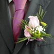 The subtle beauty of this Stanmore buttonhole is immediately apparent, evoking both nostalgic romance and an air of joyful celebration along the leafy streets of northwest London. Resting gracefully atop a perfectly pressed lapel, the pastel pink rose opens with a sense of softness, its silken petals radiant in gentle, natural light. Nestled nearby, a compact, zesty green chrysanthemum adds a playful energy, balanced by delicate clouds of white gypsophila that radiate purity and affection. Fine fern tendrils and slender blades weave in a tapestry of green, their feather-light textures mirroring the tranquillity of nearby parkways and historic gardens. A shimmering lavender ribbon, tied with precision into a neat bow, unites the floral elements with the bold pink tie underneath, achieved through mindful coordination. Created for a Stanmore wedding or formal gathering, this buttonhole feels both lively and serene-a story of new beginnings, local craftsmanship, and timeless floral artistry, designed to bring a touch of personal charm to any special occasion.