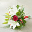 This image shows an elegant bouquet resting on a light, woven surface, positioned diagonally so the flowers sweep gracefully across the frame like a bridal posy carried through Stanmore's quiet streets. Dominating the composition are several white oriental lilies, some fully open with wide, ruffled petals that form star-like shapes, others still wrapped in smooth green buds. The open blooms reveal faint splashes of reddish speckles near their centres, adding delicate character to the creamy white. At the heart of the bouquet, a single deep red rose sits like a jewel, its tightly spiralled, velvety petals creating an immediate sense of classic romance, perfect for a proposal dinner at home. Flanking the rose are two rounded 'Green Trick' dianthus, vivid green and almost moss-like in texture, giving the arrangement a contemporary twist that contrasts beautifully with the more traditional blooms. Threaded through the design, tiny white gypsophila flowers - baby's breath - form airy clusters, softening the overall look and adding a feeling of lightness. Small clusters of red hypericum berries dot the greenery, their glossy surfaces catching the light and echoing the rose's rich hue, adding a hint of seasonal festivity. Surrounding the flowers, an abundance of foliage spills outward: deep green leaves provide structure while fine, grass-like strands curl and arc, adding movement and rhythm. The stems are gathered and wrapped close to the cut ends with a wide, shimmering red satin ribbon, tied neatly, its surface reflecting the ambient light and reinforcing the bouquet's romantic tone. The neutral background - likely an off-white or beige fabric - ensures the vivid reds, crisp whites, and fresh greens stand out clearly, making this bouquet ideal for weddings, anniversaries, or special deliveries around Stanmore and the nearby leafy avenues.