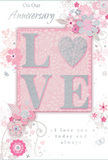 This anniversary card offers a gentle celebration of enduring romance, wrapped in soft pastel pinks and silvery greys that recall early evening skies over Stanmore. At its heart, the word LOVE appears in raised glitter lettering, each character softly contoured as though dusted with fine, luminous sugar. The O has been transformed into a silver-textured heart, shimmering with dense sparkle that contrasts beautifully against the surrounding blush tones, much like a single statement bloom in a modest, pastel bouquet. Around this central word, delicate blossoms in blush, mauve, and muted rose open across the card with a watercolour fluidity. Their petals are rendered with subtle gradients and gentle lines, giving an impression of movement and softness, as if they had just been arranged by hand on a table in a Stanmore kitchen. Slender stems, looping vines, and small leaf clusters weave between the flowers, guiding the eye in sweeping curves from corner to corner. Tiny details - curled petals, subtle butterflies, and fine swirling flourishes - add a sense of whimsy and light, reminiscent of a breezy walk through Canons Park in springtime. Above or below the floral display, phrases such as On Our Anniversary and I love you today and always are written in an understated, graceful script that feels warm and personal, like words spoken quietly over a shared meal at home. The composition is airy yet emotionally full, balancing negative space with detailed illustration so that nothing feels heavy or overstated. Overall, the card captures the spirit of a tender, long-lasting partnership, much like the thoughtful bouquets delivered across Stanmore to mark precious milestones and cherished years together.